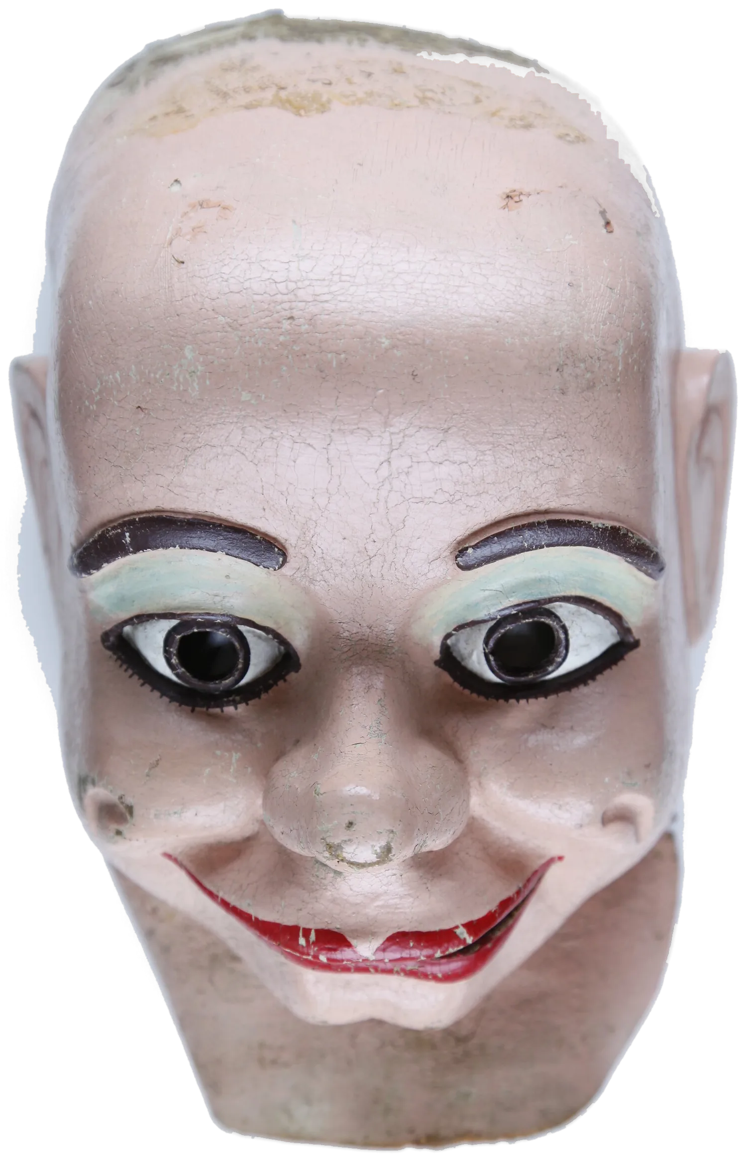 A painted rubber mask of a ventriloquist’s doll’s face: bald pink head, heavy black brows, round eyes, a wide red grin, the paint cracked all over.